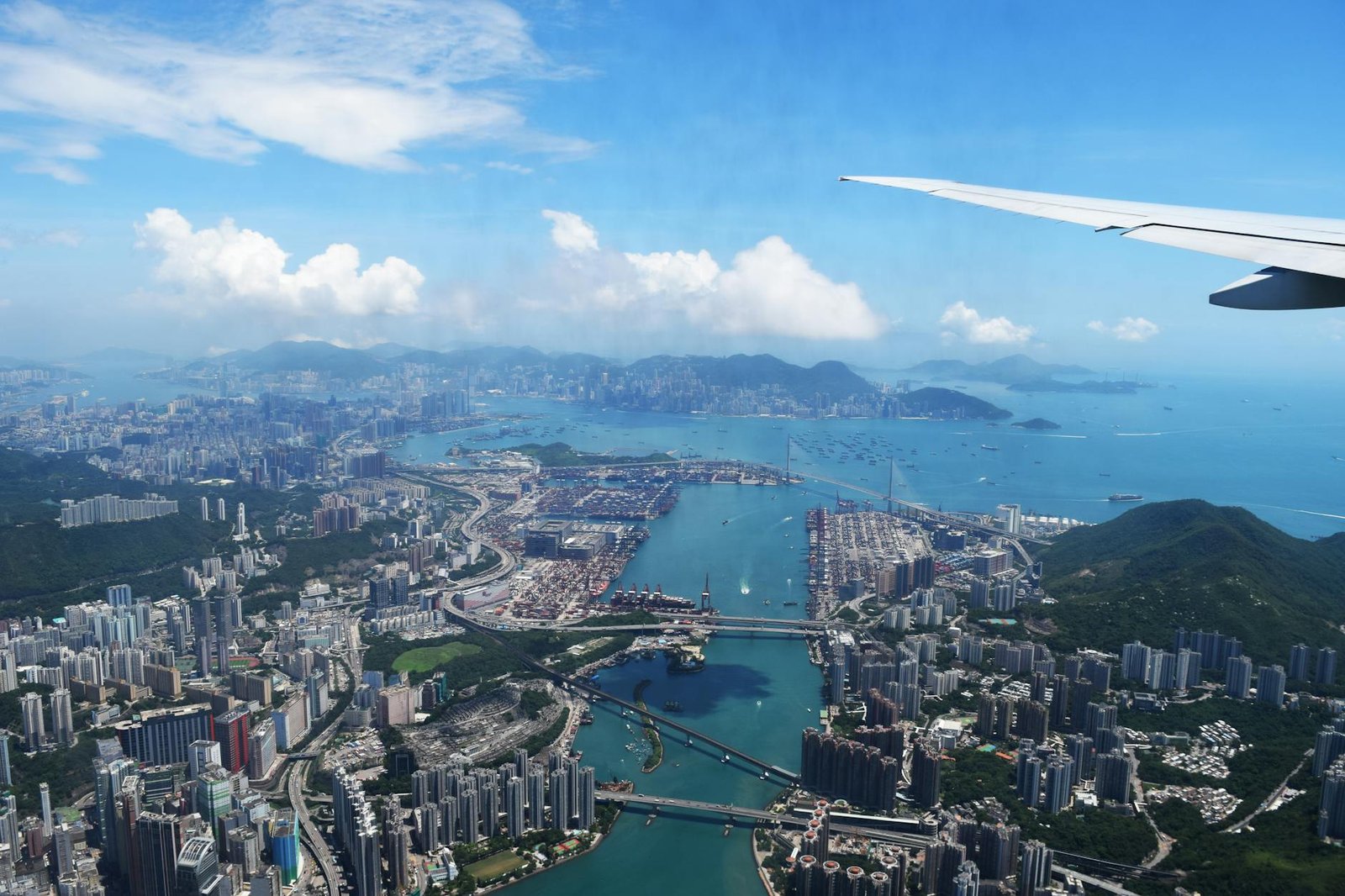 Stunning aerial view over Hong Kong with cityscape and ocean, featuring an airplane wing.