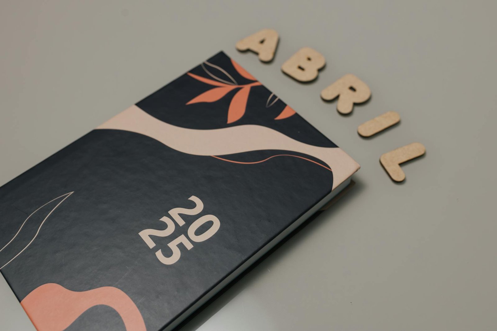 Elegant 2025 planner with abstract cover and wooden letters spelling Abril on a gray surface.