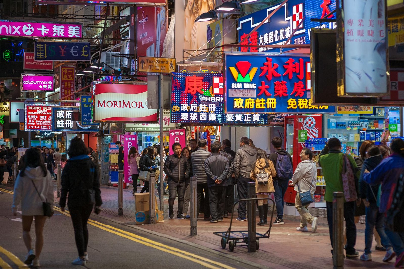 Bustling street scene on Hong Kong Island with neon lights and crowded sidewalks at night.