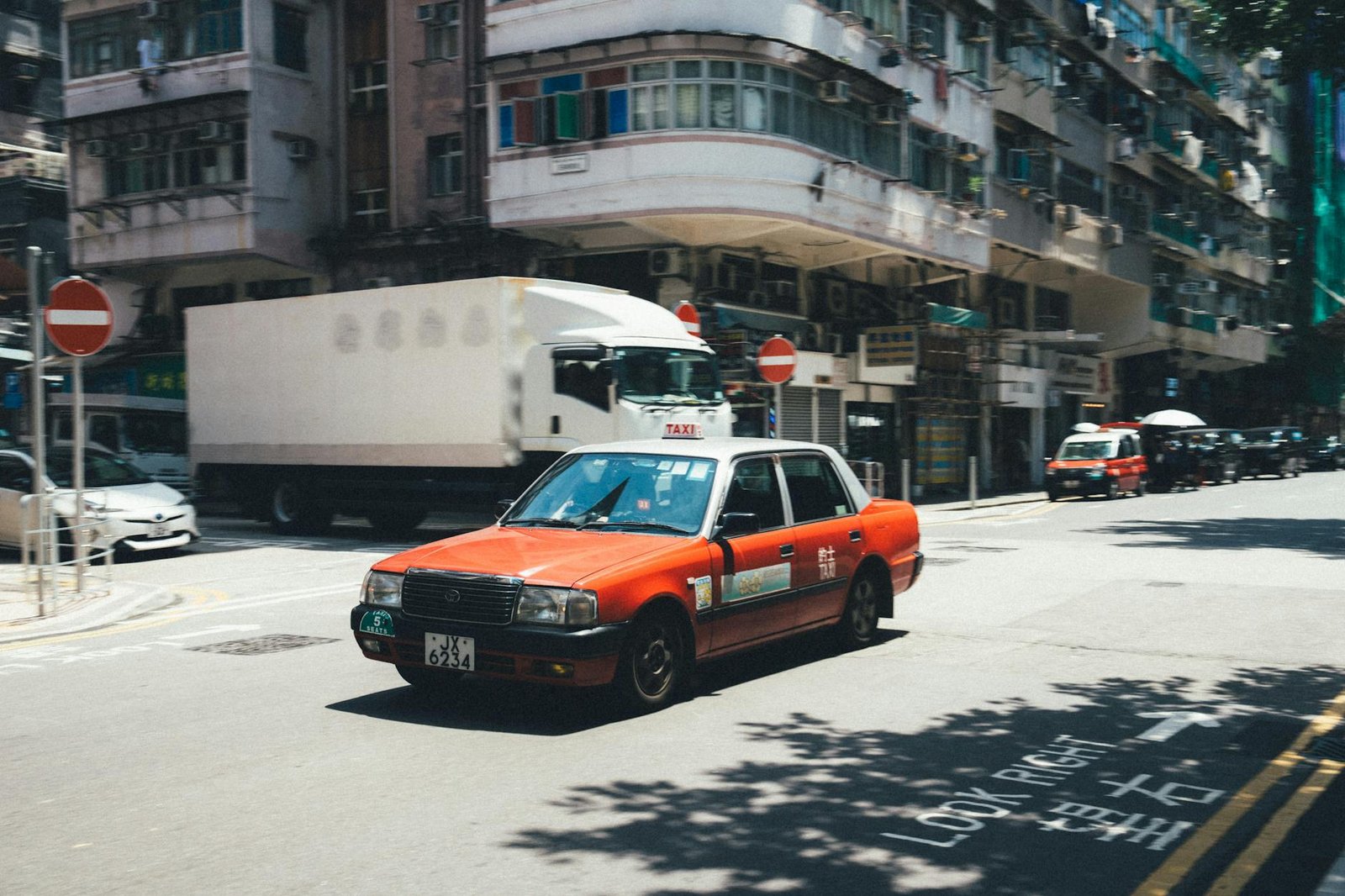 A red taxi turns a corner on a busy street in Hong Kong, showcasing urban life and architecture.