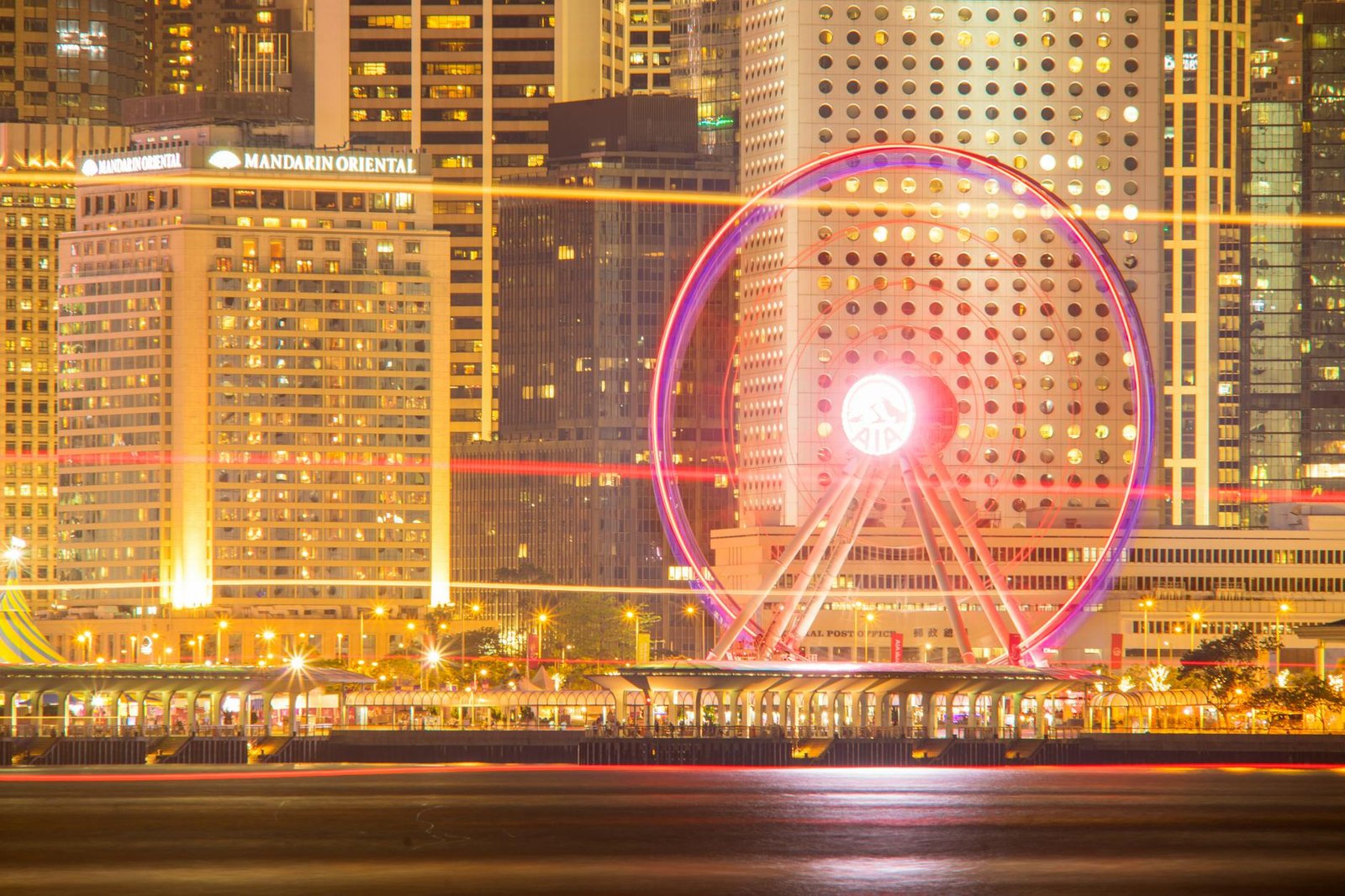 Hong Kong skyline at night featuring the illuminated Ferris wheel and skyscrapers.