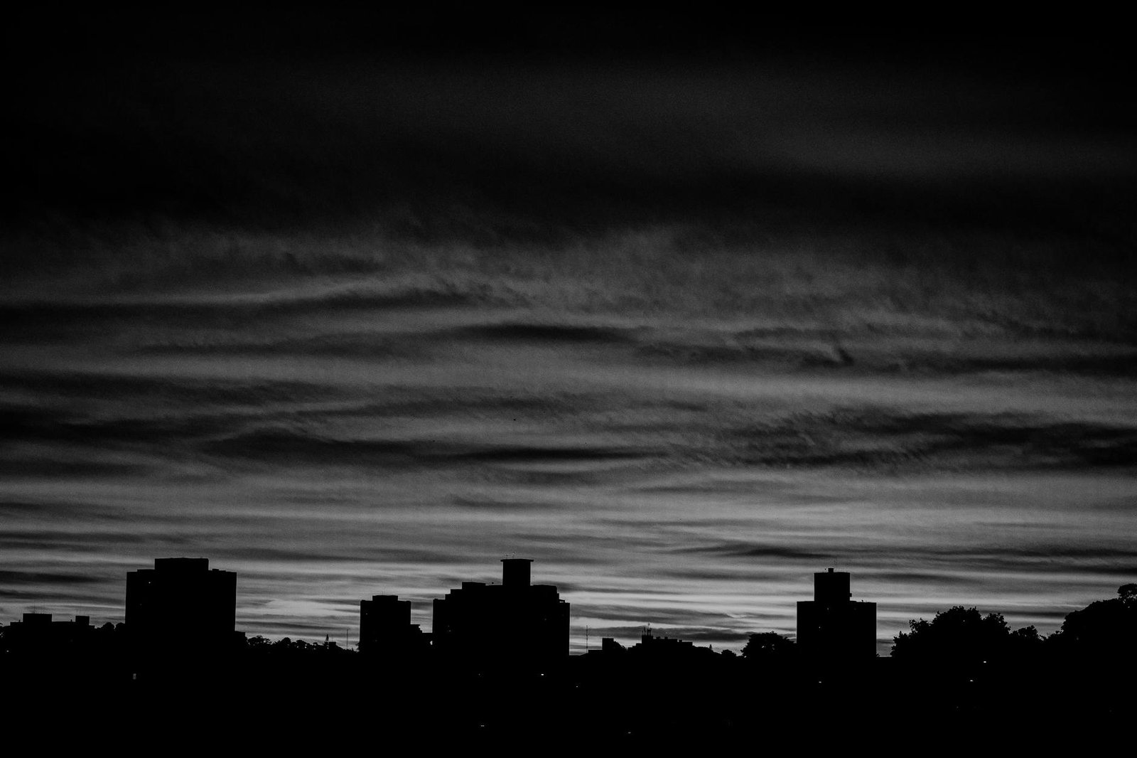 A dramatic black and white city skyline silhouette with a moody twilight sky.