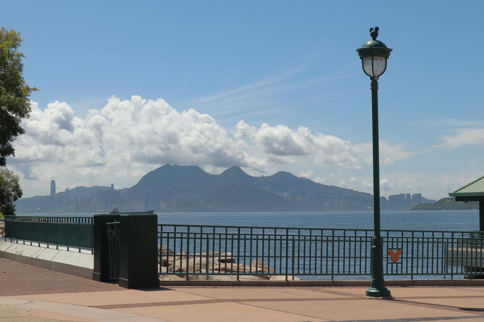 Peaceful view of Hong Kong skyline from a waterfront walkway on a sunny day.
