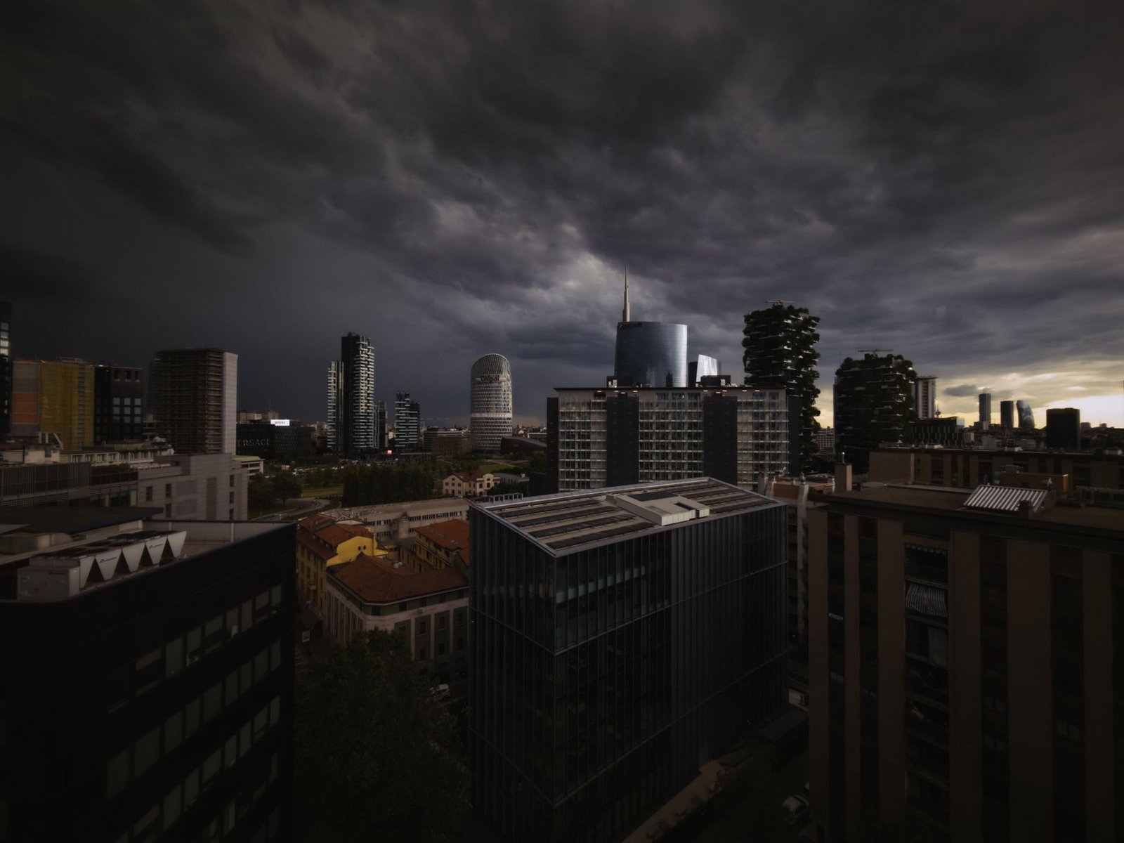 A dark, stormy sky looms over a modern urban skyline at dusk, creating a dramatic cityscape.